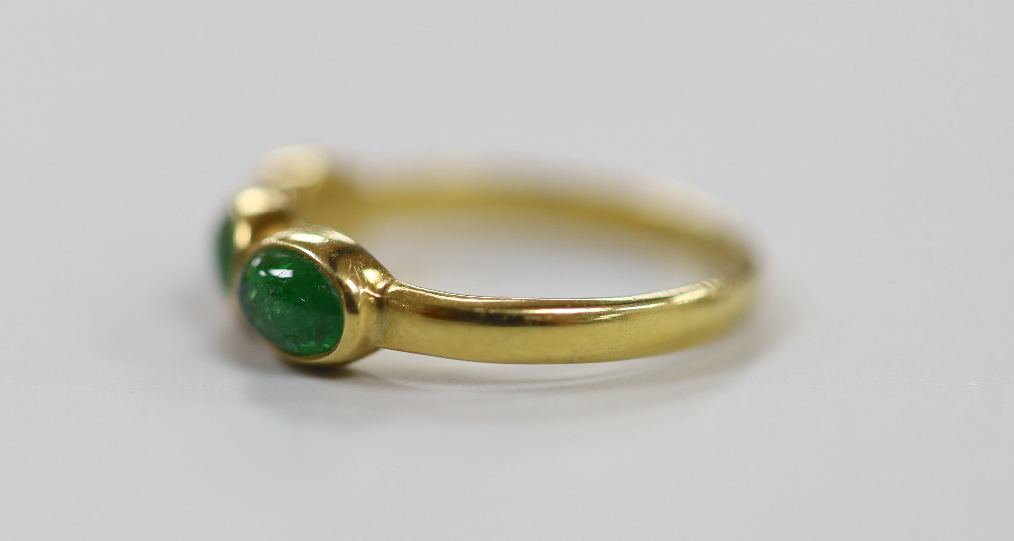 A modern 18ct gold and three stone cabochon emerald set half hoop ring, size N, gross weight 3.2 grams.